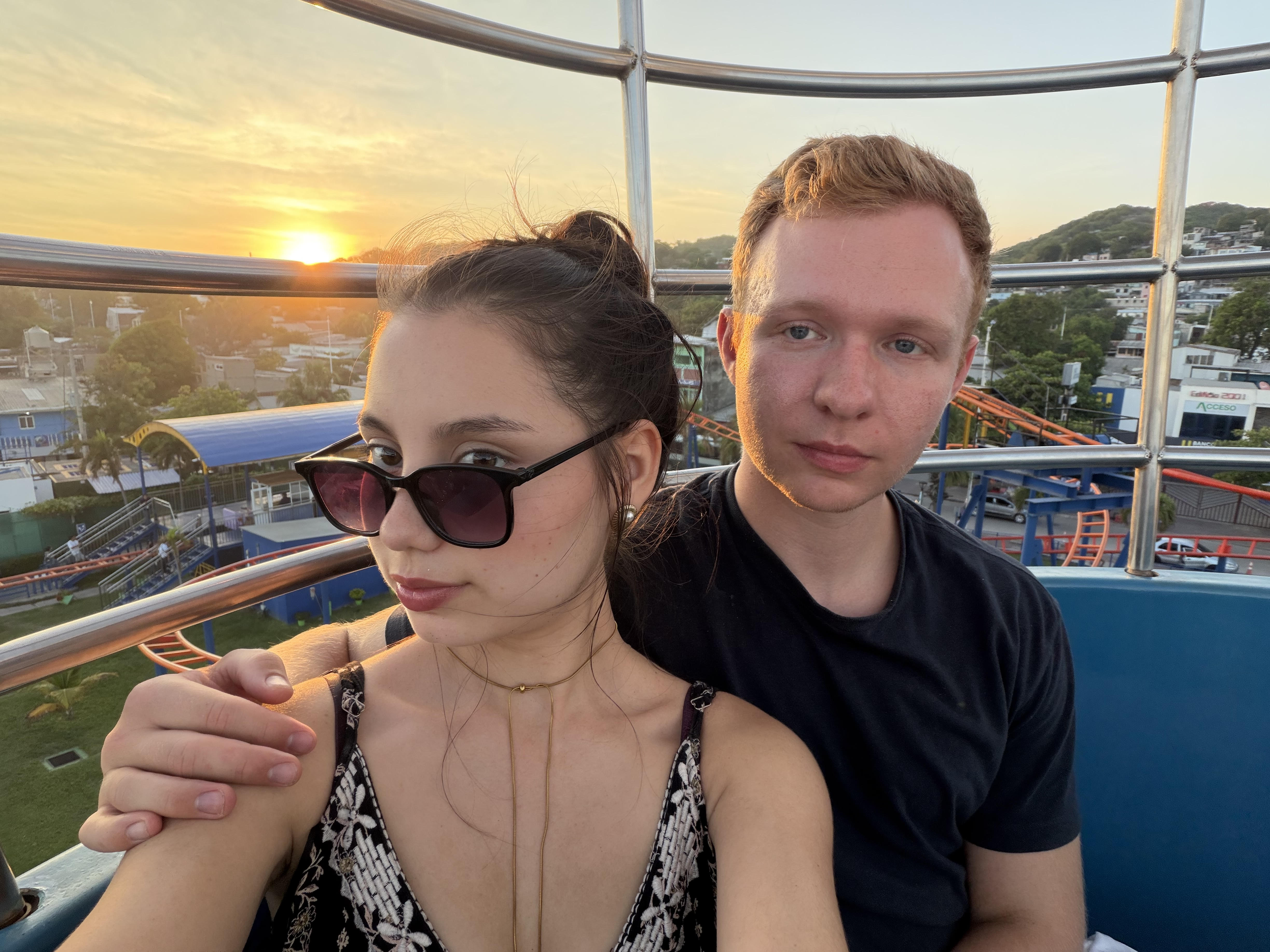 A couple selfie on a Ferris wheel at sunset with an amusement park below
