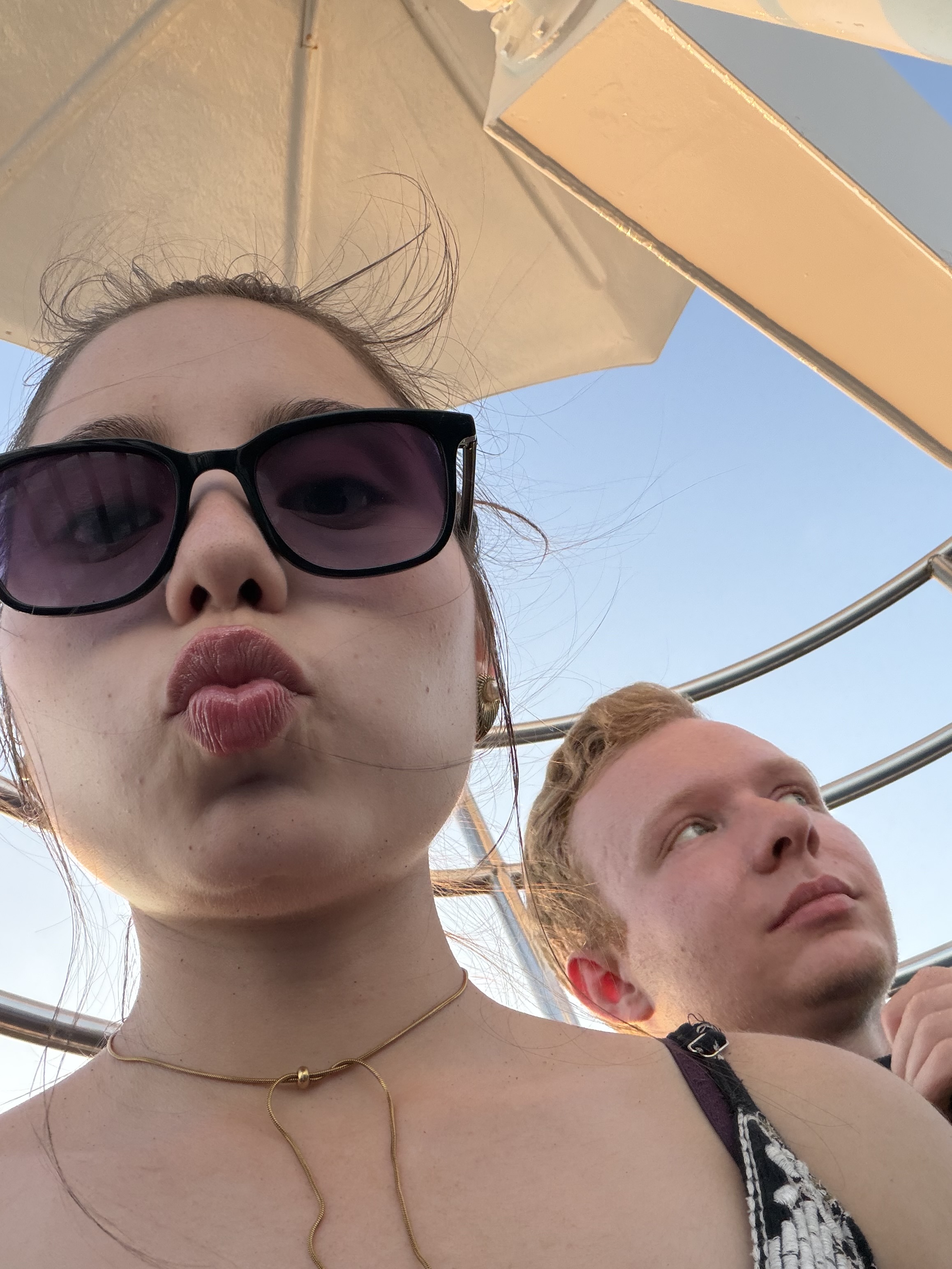 A sunny selfie under a beach umbrella making a kiss face